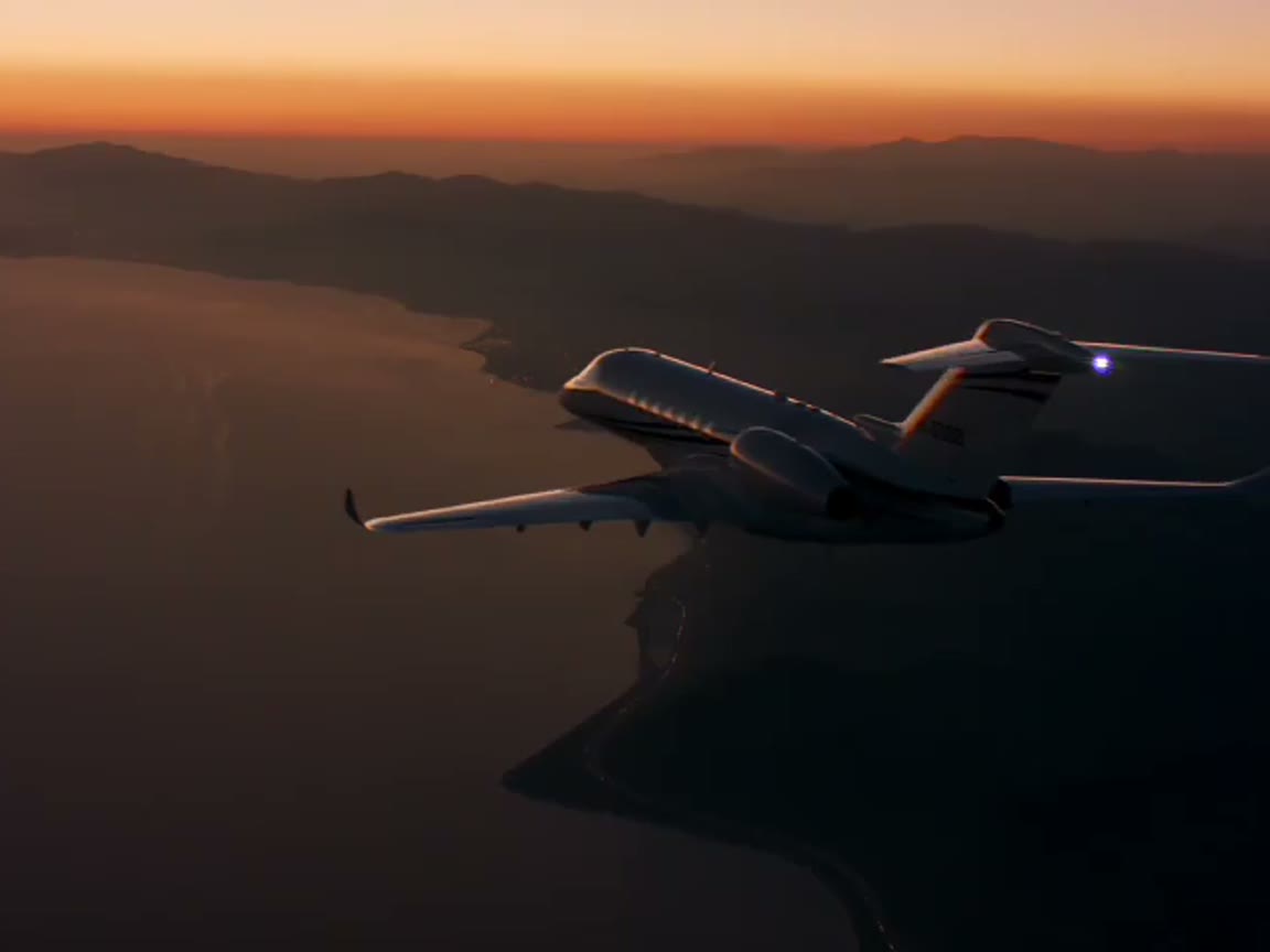 A small aircraft gliding above a coast at sunset